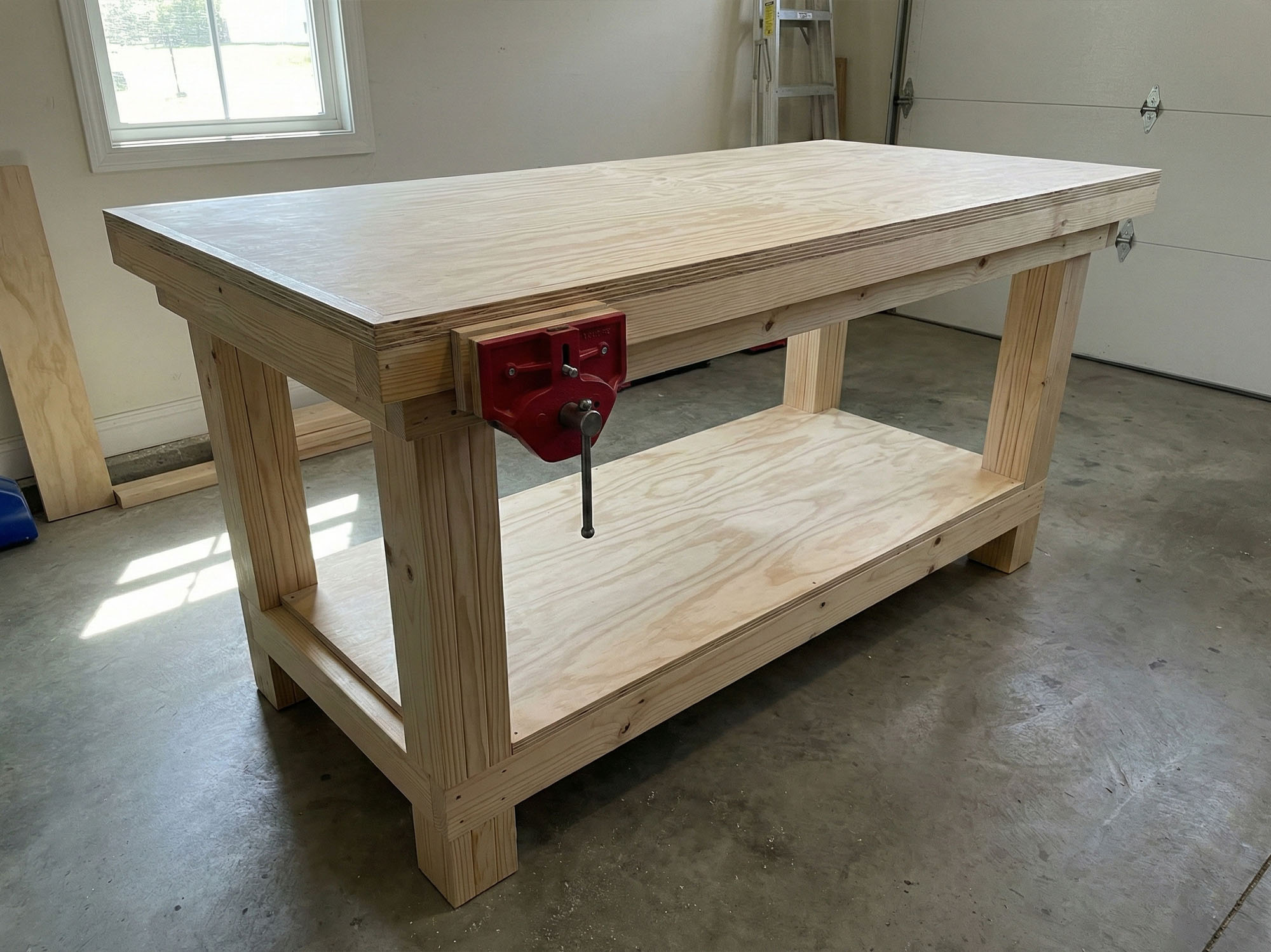 A finished, heavy-duty DIY wooden workbench in a garage featuring a double-layered plywood top, a lower storage shelf, and a red metal woodworking vise.