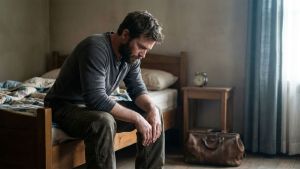Man sitting on edge of bed in early morning light, reflecting the weight of sleep deprivation and stress on male health