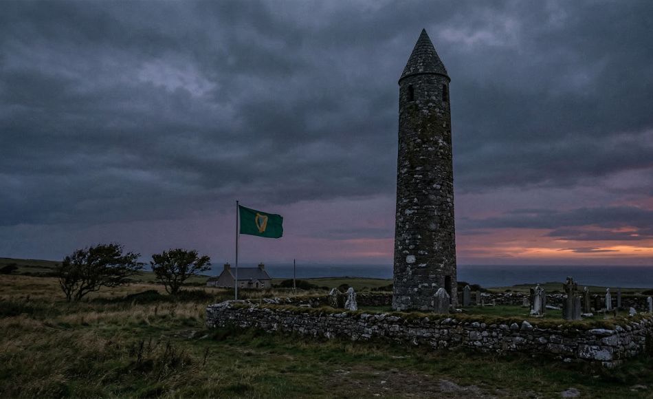 Torre de pedra irlandesa antiga sob céu tempestuoso, representando a herança irlandesa e o espírito celta