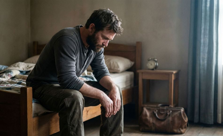 Man sitting on edge of bed in early morning light, reflecting the weight of sleep deprivation and stress on male health