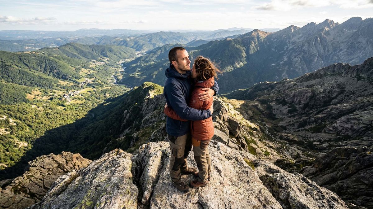 Un homme et une femme sur un sommet rocheux, symbolisant un partenariat malgré des perspectives différentes.