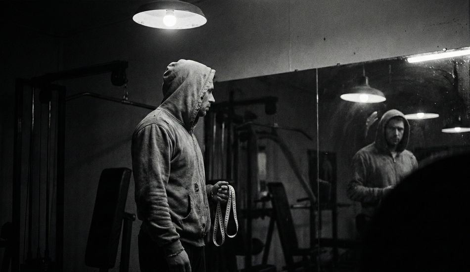 A man examining his reflection, symbolizing the pressure of male physical statistics.