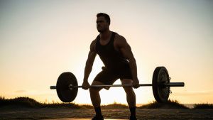 Man lifting barbell at sunrise with strong posture and focused expression