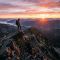 A man standing on a rocky mountain peak overlooking a vast valley at sunrise.