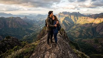 Homem e mulher em um pico rochoso simbolizando parceria com perspectivas diferentes.