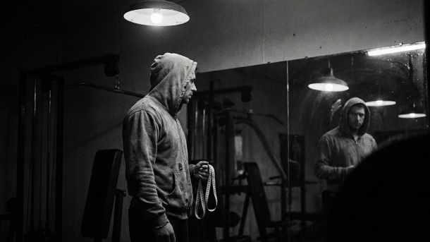 鏡の中の自分を見つめる男性。男性の身体統計によるプレッシャーを象徴している。