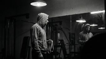 A man examining his reflection, symbolizing the pressure of male physical statistics.