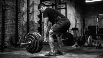 Hombre realizando un levantamiento de peso muerto con barra pesada con soporte corporal completo, lo que representa la activación del suelo pélvico y la estabilidad del tronco en atletas masculinos.