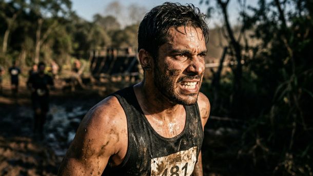 Homem competindo sozinho em um desafio físico exigente, incorporando o impulso bruto e a conquista merecida