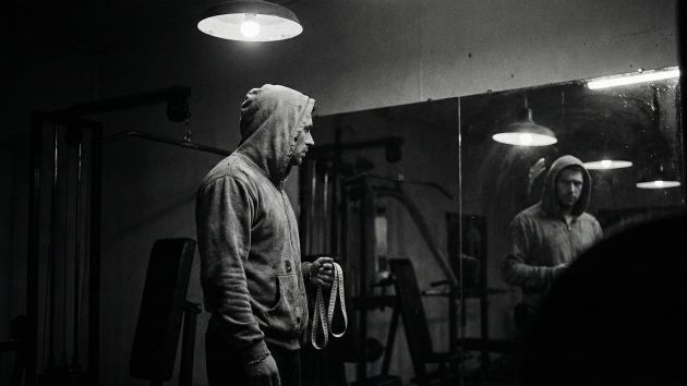 Un hombre examinando su reflejo, simbolizando la presión de las estadísticas físicas masculinas.