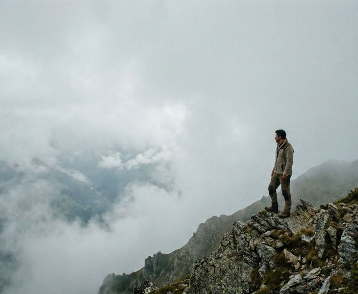 Un hombre parado solo en una cresta de montaña neblinosa y escarpada, evitando preocupaciones médicas.