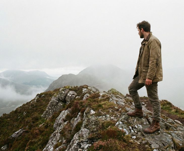 Ein Mann steht allein auf einem nebligen, zerklüfteten Berggrat und meidet medizinische Sorgen.